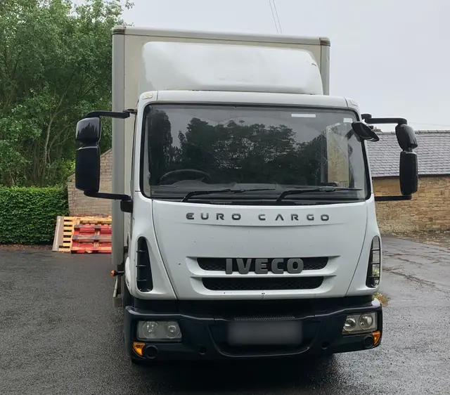 Front view of a white Iveco Eurocargo box lorry parked on a wet yard before a removal