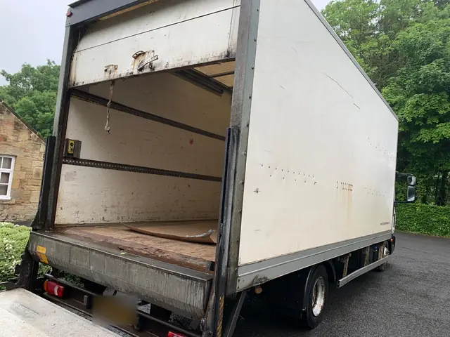 Large white box lorry with its rear shutter open and the tail lift lowered, ready to load a house clearance