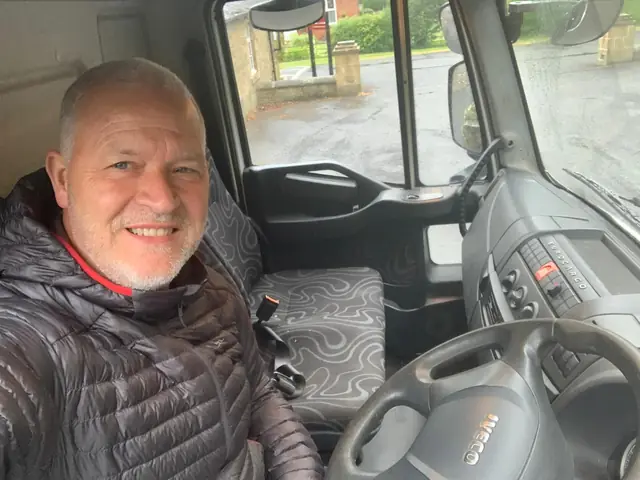Smiling We Shift driver with grey hair in the cab of a removal lorry, ready for the day's move