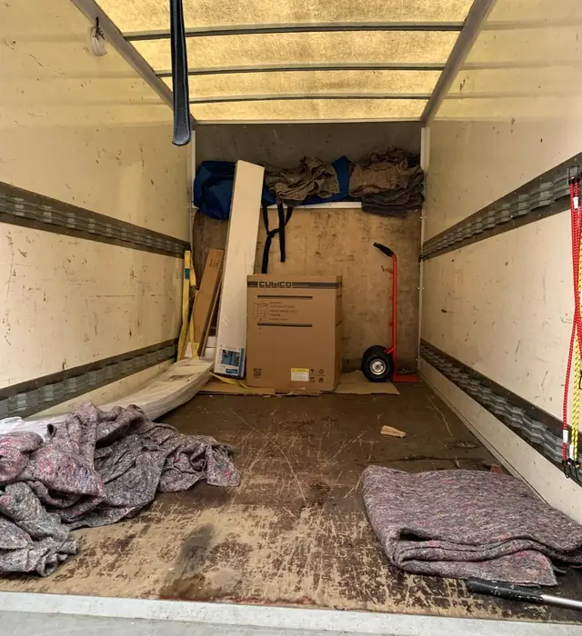 Removal blankets on the floor of a Luton van, with a sack truck and a boxed item at the far end